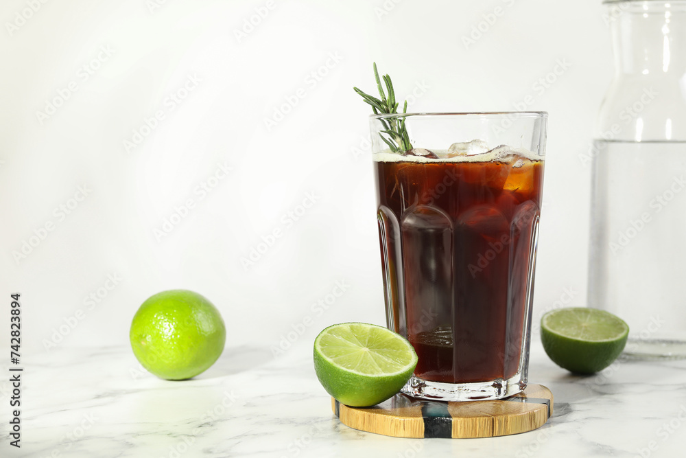 Wall mural Refreshing iced coffee with rosemary in glass and fresh limes on white marble table, space for text