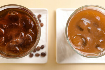 Refreshing iced coffee with milk in glasses on beige table, flat lay