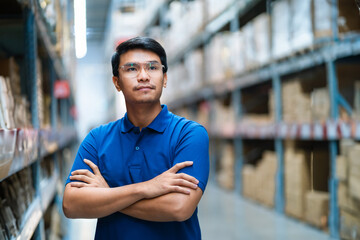 Asian male worker in a large warehouse inspects cardboard boxes in a logistics distribution center....