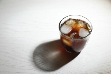 Refreshing iced coffee in glass on white wooden table. Space for text
