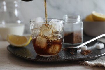 Pouring coffee into glass with ice cubes at white wooden table, closeup