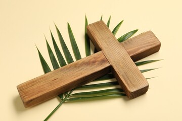 Wooden cross and palm leaf on beige background. Easter attributes