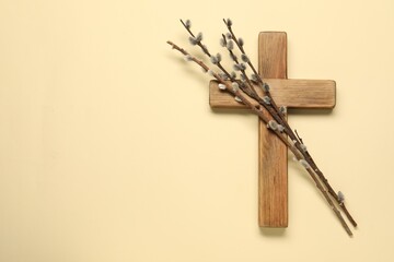 Wooden cross and willow branches on beige background, top view with space for text. Easter...