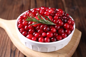 Fresh ripe cranberries and rosemary in bowl on wooden table, closeup