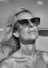 Close up shot of happy blonde woman wearing sun glasses looks up black and white