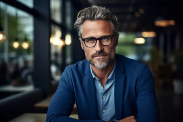 Foto op Plexiglas Business man with a confident stare and stylish glasses, dressed in a smart blue blazer over a casual shirt, sits in a cafe. Successful entrepreneur, experienced professional and business environments © Darya