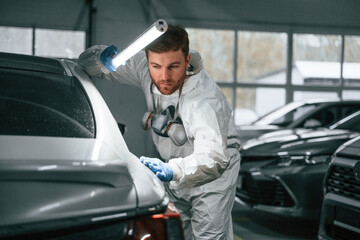 Searching for imperfections. Garage worker is holding lighting and checking surface of the car