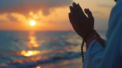 Muslim man with rosary beads praying at sunset on ocean background
