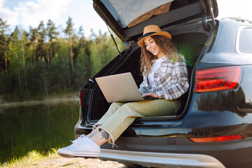 Happy woman with laptop sitting in car trunk. Remote work. Business, blogging, freelance, Online...