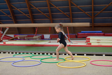 A small girl runs through hula hoops in the gym