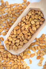 Fenugreek seeds with wooden spoon on mottled grey surface