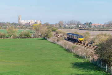 Railway train flanked by fields and ancient minster on horizon under blue sky. Beverley, UK.