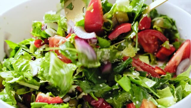 Mixing a fresh vegetables salad. Salad bowl of romaine lettuce, arugula, tomato, paprika, red onions, olives and dressing with olive oil. Stock footage video 4k