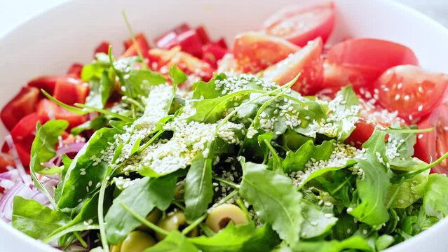 Mixing a fresh vegetables salad. Salad bowl of romaine lettuce, arugula, tomato, paprika, red onions, olives and dressing with olive oil. Stock footage video 4k