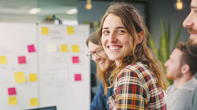 Smiling young woman in a creative office space, colleagues in soft focus behind her.