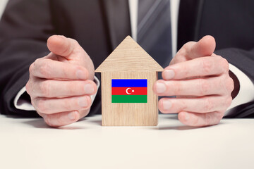 Businessman hand holding wooden Home model with Azerbaidjani flag. insurance and property concepts