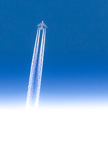 Airplane seen from below with white contrails in a clear blue sky with gradient from blue to white with copy-space