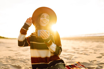Young woman drinking morning coffee at picnic on the beach. Travel, weekend, relax and lifestyle concept.