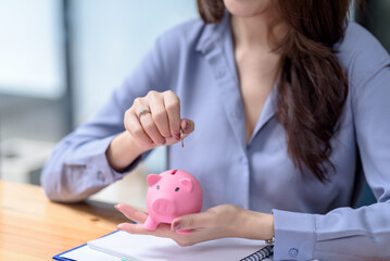 Professional saving money concept with a woman inserting coin into a piggy bank. Financial planning...