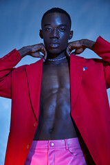 handsome stylish african american man in pink pants and red blazer posing on blue watery backdrop