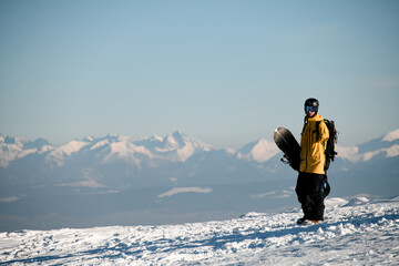 Male snowboarder standing on sunny day against backdrop of beautiful mountain peaks shrouded in fog