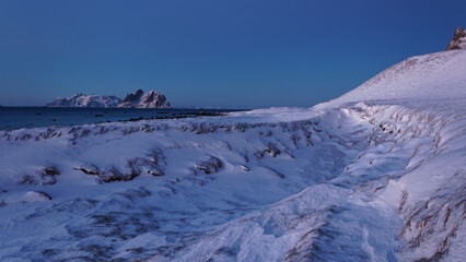 Snow-covered natural ditch by the rocky coast, with mountainous neighbouring islands in the...