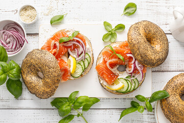 Salmon sandwiches with bagel, salted fish, fresh cucumber, onion and basil on white background, top view. Healthy breakfast with salmon toasts