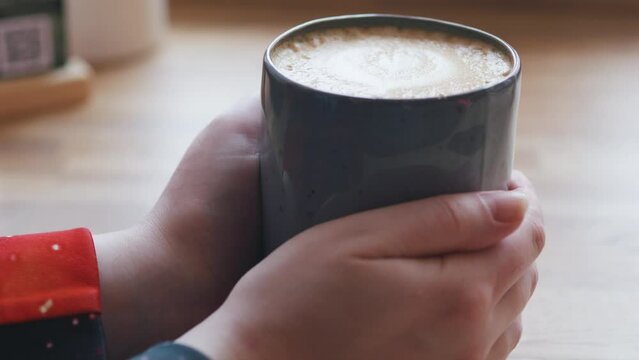 Female hands holding mug of cappuccino coffee. Wooden table. Coffee shop.