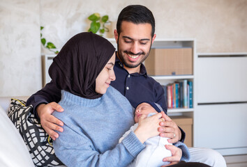 Arabic Muslim parents share a tender moment with their newborn daughter, radiating love and joy in their home.