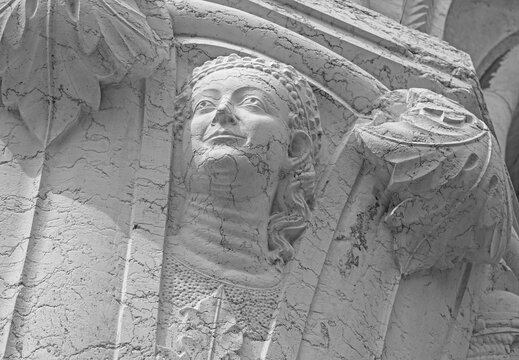 Venice, Italy, Sept. 17, 2023: Closeup head of a genteel woman in stylish hat and dress shows the artistry of the medieval stone carvings on the Doge’s Palace portico columns.