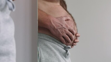 Reflection in the mirror of male belly, overweight. Man with bare fat belly shakes fat folds on his stomach, obesity, health, beer belly. Problem area of body. Hormones. Copy space