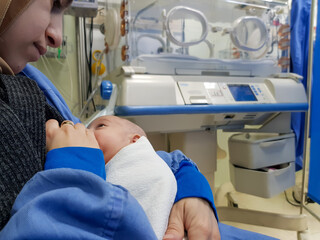 mother holding her baby for breastfeeding beside the incubator in hospital in PREMATURITY room to give her baby the best nutrients
