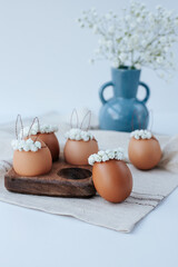 On a linen napkin there is a wooden egg cup with brown Easter eggs with flower wreaths and bunny...