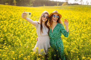 Two woman takes a selfie while walking flowering field. Fashion, beauty concept. Summer landscape.