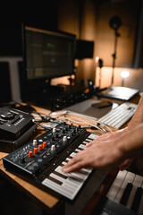 Fototapeta na wymiar In the recording studio, professional equipment is located on the table, male hands press the keys of the hybrid synthesizer