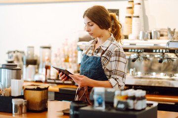 Smiling female barista takes an order from a tablet while standing at the bar counter in a coffee shop. Online order. Small business, people, takeaway and service concept. - Powered by Adobe