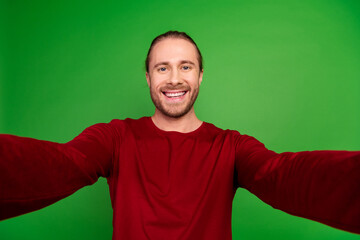 Fototapeta premium Portrait of toothy beaming handsome guy with long hairstyle wear red sweatshirt smile on selfie isolated on green color background