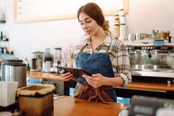 Smiling female barista takes an order from a tablet while standing at the bar counter in a coffee...