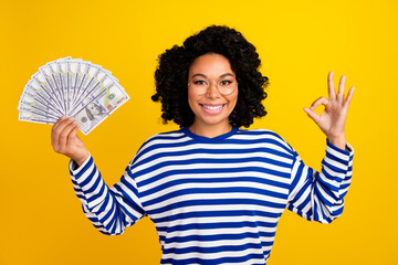 Portrait of multinational good mood nice girl with chevelure in glasses hold money showing okey...
