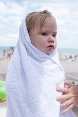 little one year old wet girl wrapped in a towel on the beach