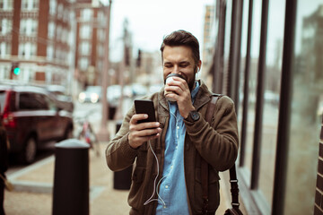 Smiling Man Texting on Smartphone and Holding Coffee on City Street