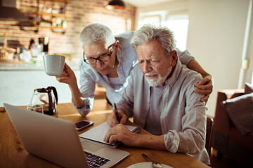 Senior man and woman reviewing documents and using laptop at home - Powered by Adobe