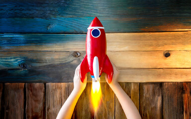 Kleine Rakete, gehalten von Kinderhänden auf Holztisch 