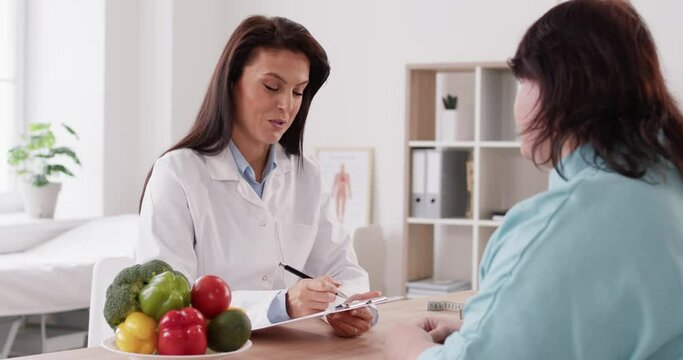 Dietician, female nutrition specialist consulting, developing healthy diet, dietary programme. Dietary consultant asking, giving overweight patient advice, help, nutritional information, new meal plan
