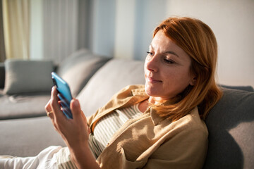 Woman smiling while browsing her smartphone at home