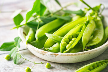 Fresh green peas in bowl with pods and leaves on white wooden table, healthy green vegetable or...