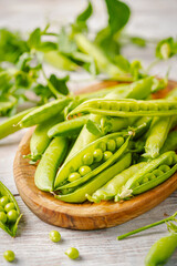 Fresh green peas in wooden bowl with pods and leaves on white wooden table, healthy green vegetable or legume