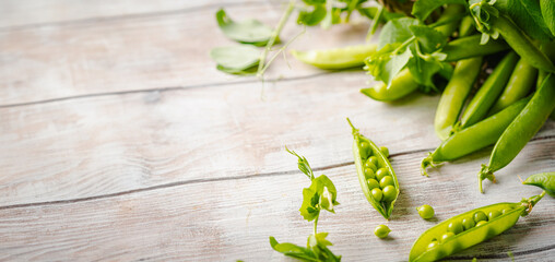 Fresh green peas in a basket with pods and leaves on white wooden table, healthy green vegetable or legume