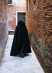 anonymous hooded stroller with black cloak dress walking through the alleys