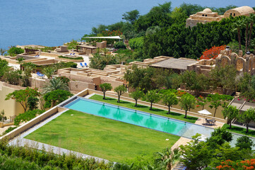 View of hotel Kempinski Ishtar Dead Sea in Jordan. Emerald water surface of pools and palm trees. Concept of tourism, recreation and treatment. Dead Sea, Jordan - May 22, 2011